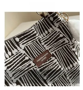 Detail of geometric woven tote bag featuring a leather logo patch and fuzzy pom pom charm