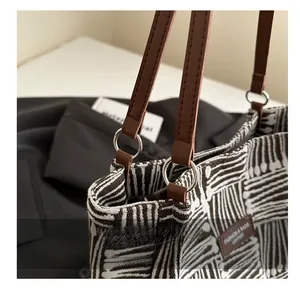 Detail of silver metal ring connecting brown leather handle to striped canvas tote bag