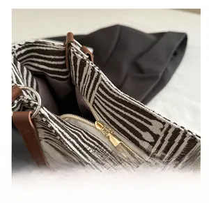 Detail of smooth metal zipper and brown leather trim on striped canvas tote bag
