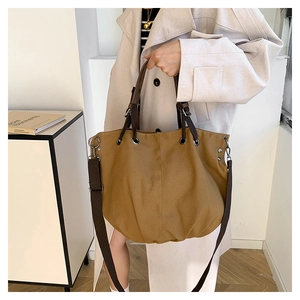 Detail of earth-tone canvas tote bag featuring brown fabric handles and metal rivets