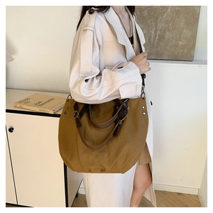 Brown canvas tote bag with leather handles and metallic rivets shown on shoulder