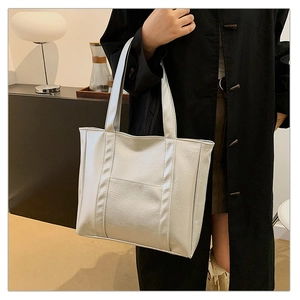 Detail of silver tote bag with lychee texture and front pocket shown on black coat