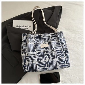 Detail of canvas tote bag with blue geometric pattern, leather handles, and office props