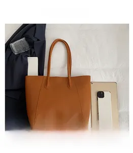 Top view of caramel leather tote bag with iPad and essentials on textured fabric