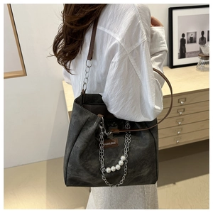 Detail of grey canvas tote bag featuring brown leather strap and decorative silver chain
