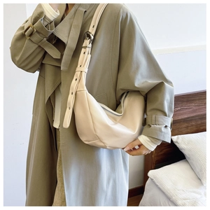 Close-up of beige crescent shoulder bag with adjustable strap worn on khaki trench coat