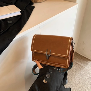 Detail of vintage brown leather handbag featuring gold studs and printed crossbody strap
