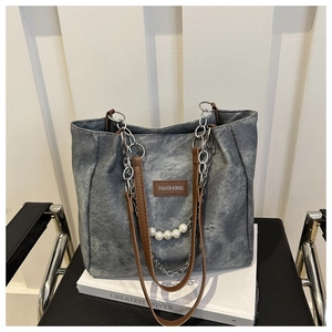 Close-up of vintage denim tote bag with leather tag, pearl chain, and silver metal links