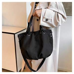 Detailed view of black canvas tote bag with metal eyelets held by model in trench coat