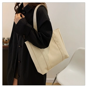Minimalist cream tote bag in textured faux leather shown on shoulder for daily commute