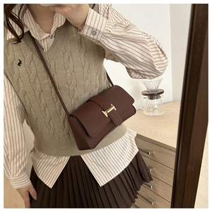 Detail of dark brown leather crossbody bag featuring a golden H-shaped metal buckle