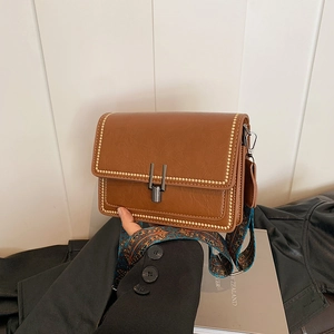 Detail of brown faux leather bag with gold rivets and colorful geometric strap