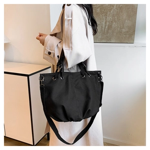 Detail of black canvas tote bag with metal eyelets worn by a model in a minimalist room