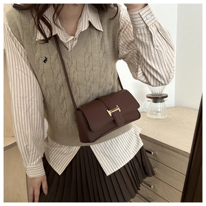 Brown leather baguette bag with metal H-buckle worn as a crossbody over a striped outfit