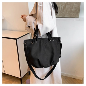 Detail of black canvas tote bag with metal eyelets and adjustable strap shown on model
