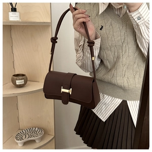 Close-up of a dark brown leather shoulder bag with a gold H-clasp and knot strap detail
