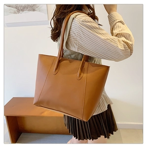 Brown leather tote bag featuring elegant stitching detail on a model's shoulder