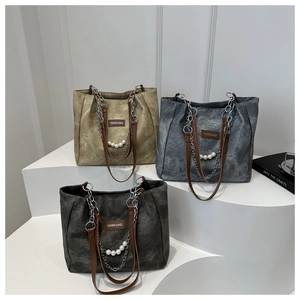 Three large canvas tote bags with chain straps and pearl charms on minimalist display