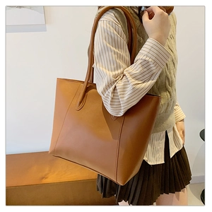 Brown leather tote bag styled on a wooden bench in a minimalist indoor setting