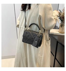 Detail of black quilted crossbody bag with FASHION embossing and mini pouch charm