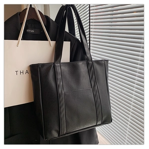 Detail of black faux leather tote bag showing fine texture and vertical decorative straps