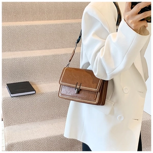 Retro brown leather crossbody bag with metal bead trim on white blazer model