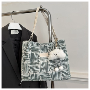 Detail of green woven tote bag with geometric patterns and cute cloud charm accessory