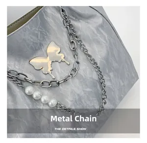 Detail of silver chain with butterfly charm and white pearls on grey textured tote bag