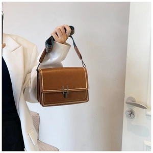 Detail of vintage brown leather crossbody bag with cream stitching and U-shaped buckle