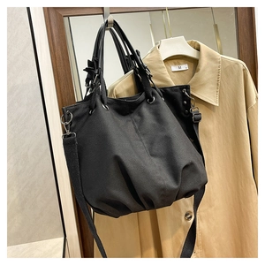 Detail of black canvas tote bag showing wide handles and adjustable crossbody shoulder strap