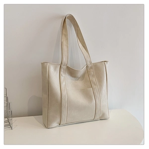 Detail of minimalist cream tote bag showing faux leather texture and front pocket