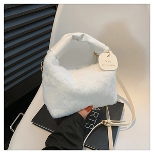 Detail of white plush handbag featuring a leather handle and engraved slogan tag