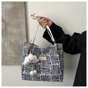 Detail of geometric canvas tote bag with white leather label and plush cloud charm pendant