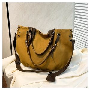 Close-up of mustard yellow canvas tote bag with brown straps and metal rivet details