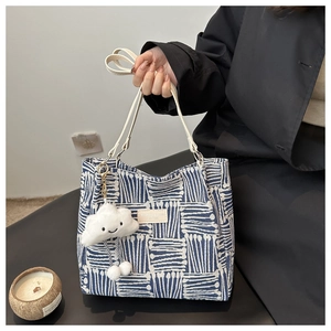 Close-up of blue geometric canvas tote with a white cloud plush charm and golden rings
