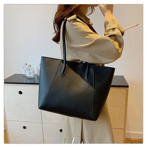 Detail of elegant black leather tote bag worn with a beige trench coat in a cozy room