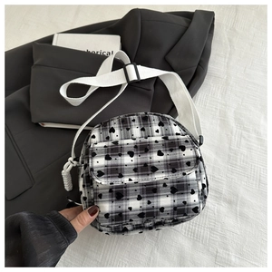 Detail of checkered canvas bag featuring black heart prints and wide woven shoulder strap