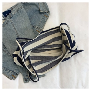 Detail view of the striped canvas tote bag with thick shoulder straps on a textured surface