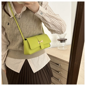 Detail of apple green crossbody bag featuring a distinctive golden H-shaped metal buckle