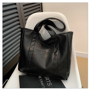Detailed close-up of glossy black PU leather tote bag with elegant stitching on a chair