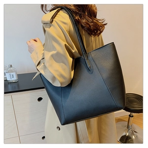 Detail of a large black faux leather tote bag with slim straps worn over the shoulder