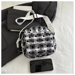 Detail of plaid mini crossbody bag with heart patterns and adjustable strap beside a phone