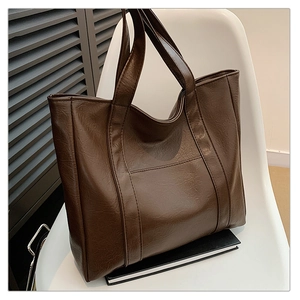 Detail of a large dark brown textured PU leather tote bag on a modern white chair