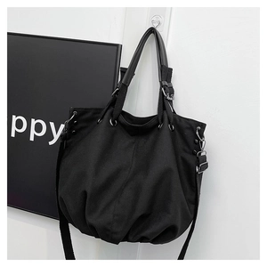 Detail of a large black canvas tote bag showing rivet accents and dual strap design