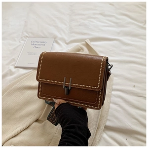 Close-up of brown leather crossbody bag with gold studs and decorative silk scarf