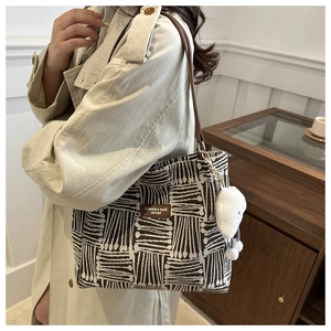 Detail of tote bag with geometric patterns, leather straps, and a plush cloud charm