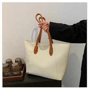 Close-up of beige tote bag with brown straps being held to show large capacity size
