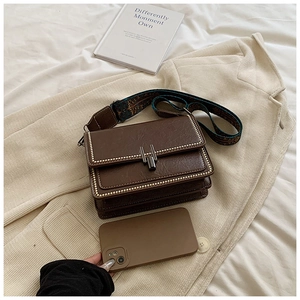 Detail of vintage brown shoulder bag with metal studs and embroidered strap shown with phone