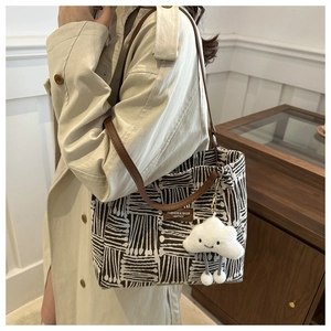 Detail of striped tote bag with leather strap and plush cloud charm on a shoulder