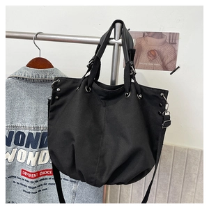 Detail of black canvas tote bag showing silver metal eyelets and adjustable strap hanging
